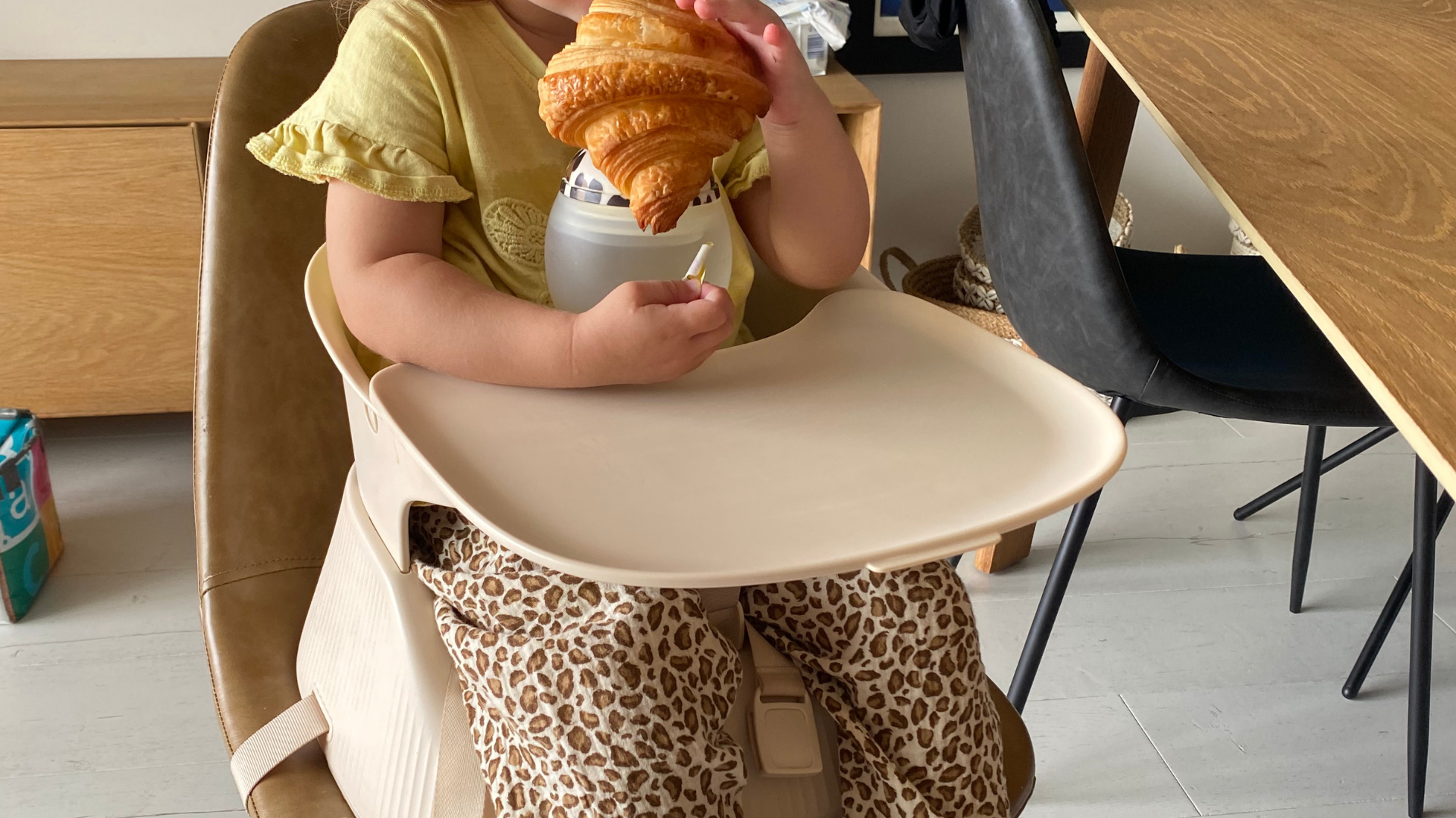 Chaise haute nomade Hannie installée sur une chaise, enfant à table sur un réhausseur portable et pliable